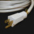 100' Triple Tap White Cord 12/3, close-up of white extension cord with multiple outlets and gold prongs on black background.