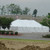 7' x 20' White Royalty Sidewall, large white event tent set up outdoors with trees and a building in the background.