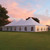 7' x 20' Cathedral Window Sidewall, large white event tent with arched windows and peaked roof set up on green lawn at sunset.