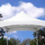 10' x 10' Pinnacle Tent Liner, a white tent liner set up underneath a large outdoor tent with a peaked roof, against a backdrop of blue sky and trees.