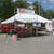 Celina Tent 20' x 20' Classic Series Pole Tent, Sectional Tent Top, Complete, outdoor event tent set up with signage, tables, and chairs in a park setting.