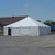 Celina Tent 30' x 30' Classic Series Pole Tent, Sectional Tent Top, Complete, outdoor event tent in white with a peaked roof, set up on pavement in a parking lot with a building and trees in the background.