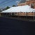 Celina Tent 30' x 60' Classic Series Pole Tent, Sectional Tent Top, Complete, set up outdoors on a paved area with a brick building and trees in the background.