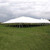 Celina Tent 80' x 100' Classic Series Pole Tent, Sectional Tent Top, Complete, large white event tent set up on grass with multiple support poles and a cloudy sky in the background.