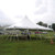Celina Tent 30' x 30' Premiere I Series High Peak Pole Tent, Sectional Tent Top, Complete, outdoor event tent with high peak design on green grass field, supported by multiple stake and pole supports, with overcast sky in background.