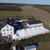 Celina Tent 40' x 120' Premiere I Series High Peak Pole Tent, Sectional Tent Top, Complete, aerial view of a large event tent set up outdoors on a green field with neighboring buildings and open land in the background.