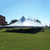 Celina Tent 40' x 160' Premiere II Series High Peak Pole Tent, Sectional Tent Top, Complete, outdoor event tent with high peak design set up on green grass with flags in the background.