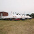 Celina Tent 40' x 180' Premiere II Series High Peak Pole Tent, Sectional Tent Top, Complete, white event tent set up outdoors with vehicles parked underneath, flags flying above, and a building in the background.