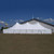 Celina Tent 40' x 80' Premiere II Series High Peak Pole Tent, Sectional Tent Top, Complete, setting up outdoors on grass with a clear blue sky in the background.