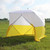 Athens Utility Shelter, portable outdoor shelter with yellow and white fabric covering on a grassy field.