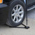 Wheel/Tire Flag Anchor Stand, close-up image showing the stand supporting a car wheel on a gravel surface.