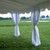 8' x 40' Leg Drape with Sash, outdoor event tent with white fabric drapes tied to tent poles, set against a green field and water background.