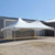 20' x 40' Pinnacle Series, White Cross Cable Tent, Complete, outdoor event tent with a white fabric canopy and cross cable support structure, set up on a paved area outside a building under a clear blue sky.