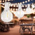25' White Bistro String Lights, close-up of hanging clear globe lights with warm LED filaments, outdoor patio dining area in the background.
