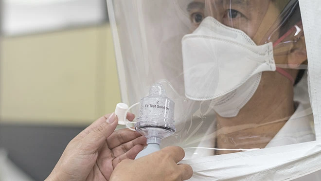 Person wearing a filtering facepiece respirator during a qualitative fit test under a test hood