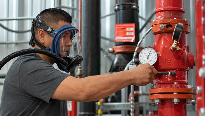 Worker wearing a full-face respirator connected to a breathing hose while maintaining industrial equipment