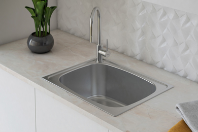 Stainless steel laundry tub and tap displayed on a clean white countertop and wall, accented with vibrant green plants.