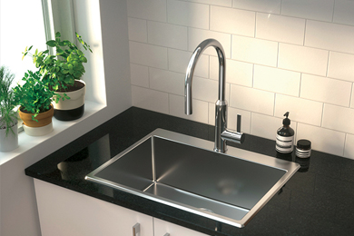 Stainless steel laundry tub and tap mounted on a black countertop, complemented by white tiled walls and green plants