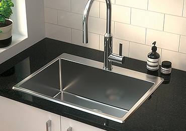 Stainless steel laundry tub and tap mounted on a black countertop, complemented by white tiled walls and a soap dispenser
