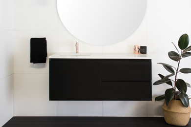 Black vanity with white countertop, against a white wall, accented by green plants.
