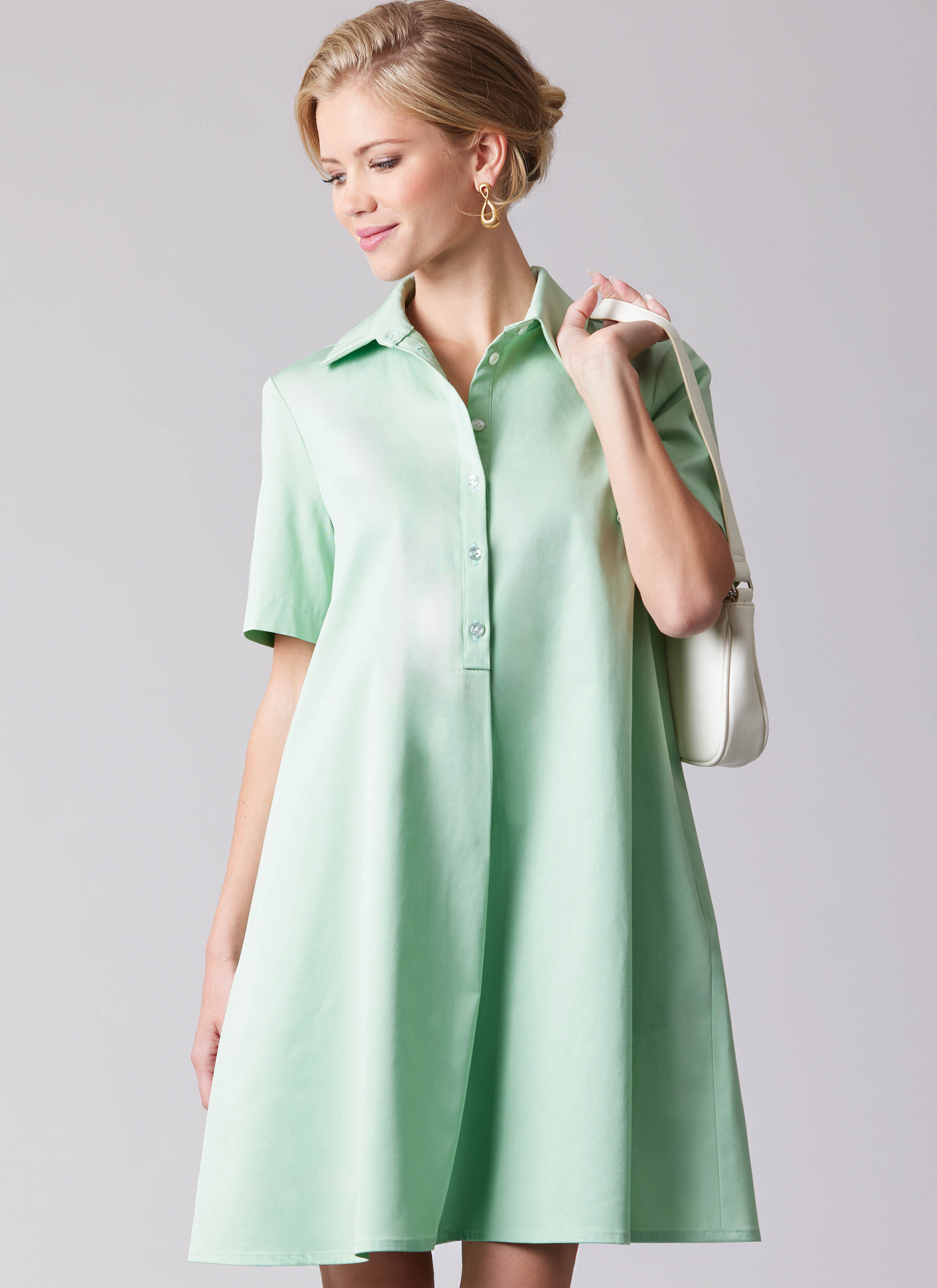 M8669 - Woman wearing green swing dress with white purse over shoulder.