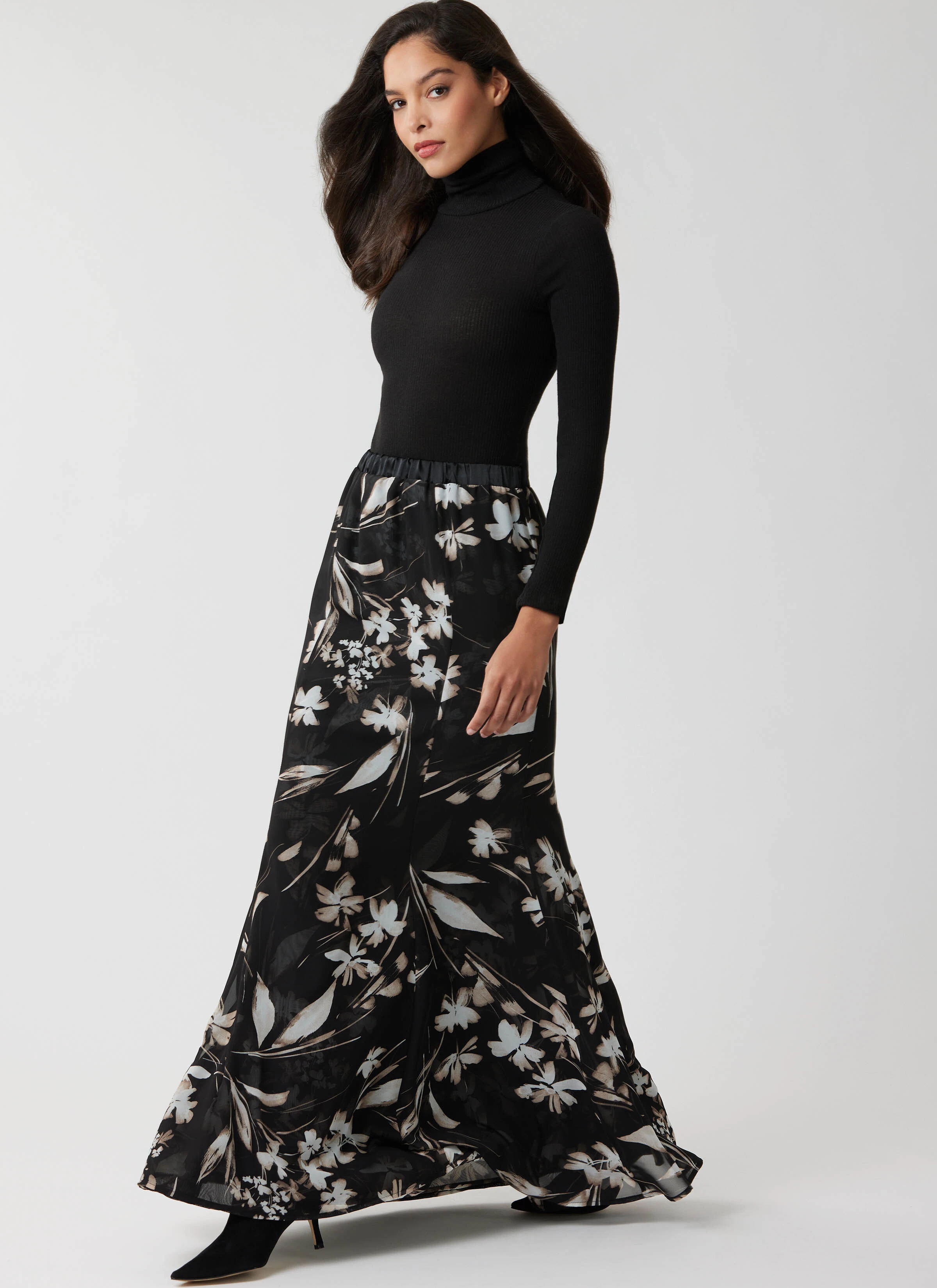 Woman wearing black maxi skirt with floral pattern and a black turtleneck.