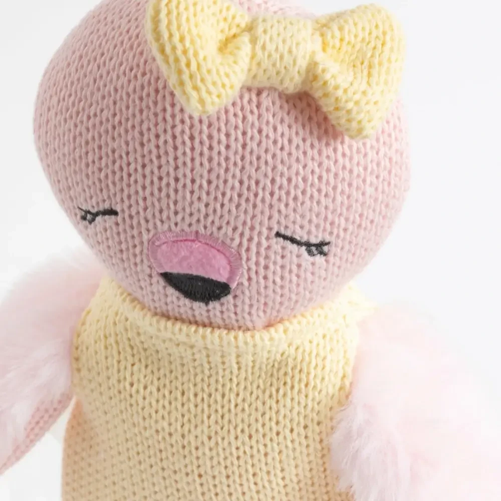 Meet Freya the Flamingo, a soft 100% cotton knitted toy with fluffy plush wings, embroidered details and a sweet yellow outfit. Perfect for cuddles and sensory play.