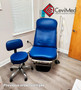 Midmark 623 barrier-free in a medical exam room with bright blue upholstery, accompanied by a matching adjustable stool on casters and nearby wall-mounted equipment.