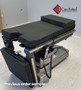 Refurbished Amsco 3085 SP Surgical Table featuring black cushions, stirrup leg section, and hand control attached to a stainless steel base