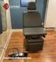 Midmark Ritter 75E refurbished chair in dark gray, placed in a medical room with wood flooring, featuring a labeled foot control with five black pedals.
