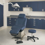 Midmark Ritter 230 Universal Power Procedures Table in dark blue upholstery, placed in a modern exam room with matching cabinetry, exam stool, overhead light, and foot control.