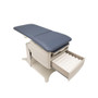 Brewer FLEX Access exam table in exam position with light blue upholstery and an open storage drawer displaying rolled paper supplies, highlighting accessible design and under-table storage.