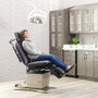 Woman sitting comfortably on a Midmark Ritter 230 power procedures table with black upholstery in a modern medical exam room, featuring overhead light and cabinetry.