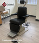 Reliance 7000 ENT exam chair with sleek black upholstery, placed in a clean, well-lit medical exam room with wood-style flooring and nearby equipment.