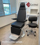Black upholstered Reliance 710 ENT examination chair with tall backrest and contoured headrest, adjustable armrests, footrest, and mounted on a round chrome and beige base, placed in a modern medical exam room.