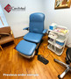 Blue Midmark 647 refurbished with armrests in a clinic room, shown with nearby equipment and wooden flooring.