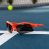 Onix Eagle pickleball glasses resting on a court line beside a tennis-style ball, dark lens visible