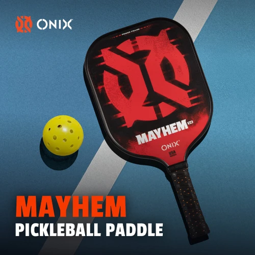 Onix Mayhem pickleball paddle lying on court with a pickleball, showing the red Mayhem face design