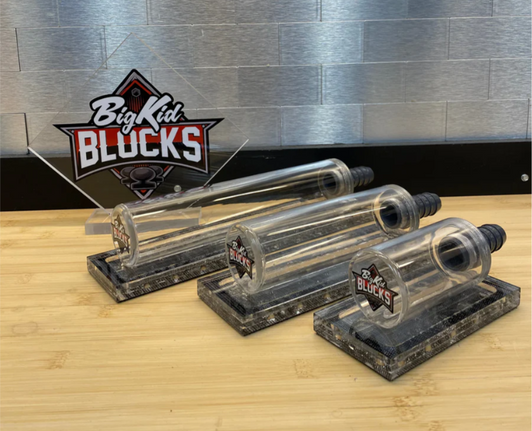Three clear Big Kid Blocks SUCK IT sanding blocks in different sizes on a wooden bench, with vacuum hose adapters and Big Kid Blocks branding displayed behind them.