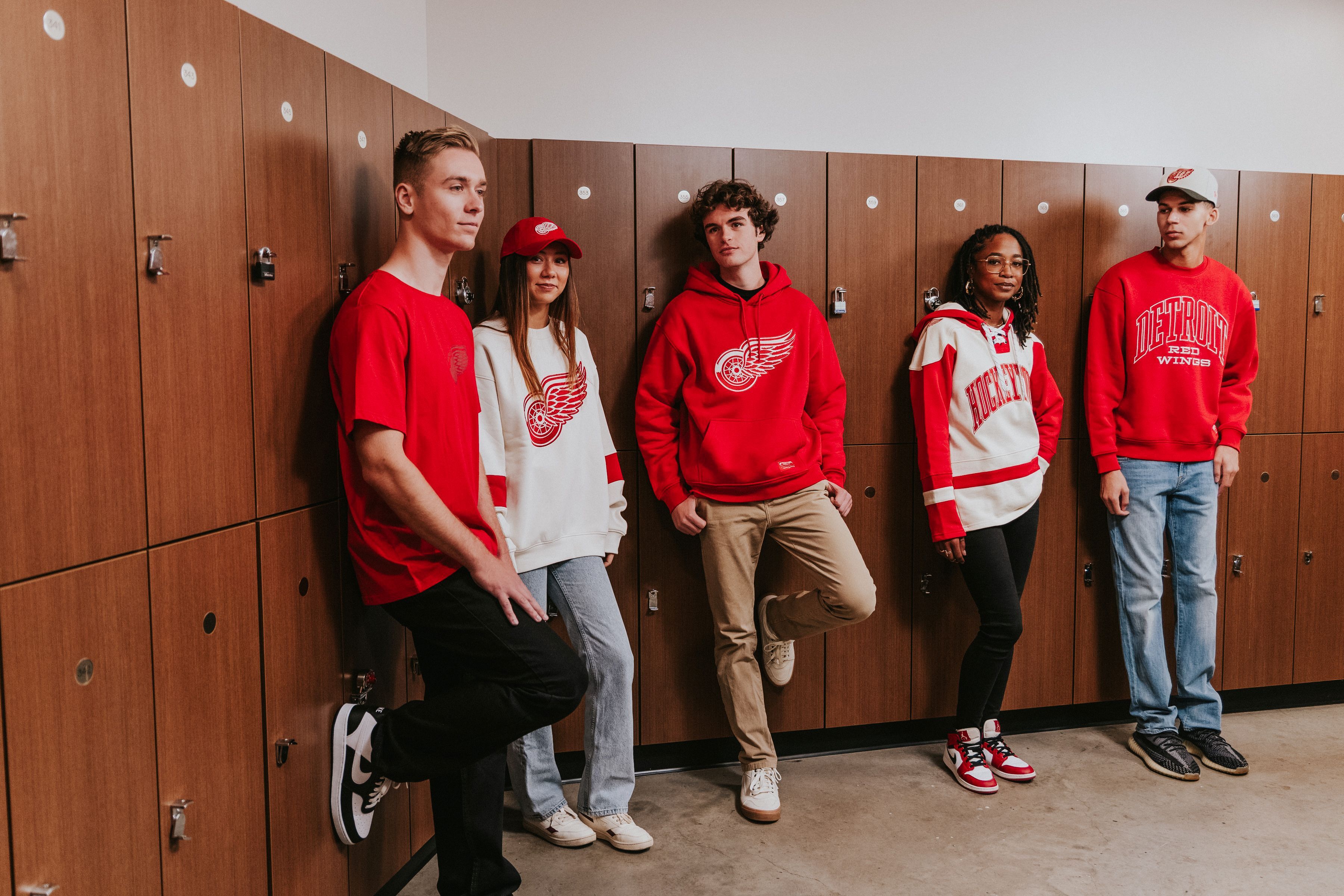 Group of adults in a locker room setting modeling exclusive Hockeytown Originals apparel. data-size=