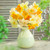 A bouquet of assorted split corona daffodils in a pale green vase, featuring flowers with white, yellow and orange petals.