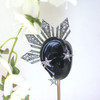 Silver Reyna Ear Cuff displayed on a black ear stand with soft white flowers in the background, creating a striking contrast that highlights its bold statement silhouette inspired by the Philippine three stars and sun. This dramatic right-ear cuff showcases regal Filipina-inspired design with an elegant, elevated presentation.