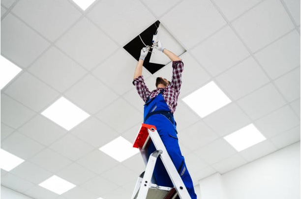 utility man on ladder handles wiring on panel fixture drop ceiling