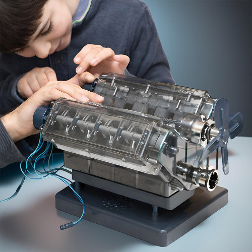 A young boy and an adult carefully assemble the V8 engine model, its transparent casing showing the internal mechanisms.