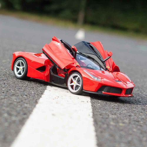 A red La Ferrari remote control car sits on a tarmac road, on a white road marker with its butterfly doors open upwards.