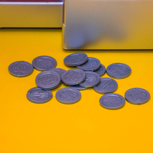 A close-up of the grey plastic toy coins for the Candy Grabber, scattered on a bright yellow surface next to the machine.