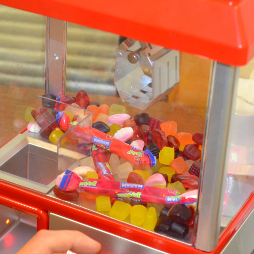 A close-up of the red Candy Grabber filled with colourful sweets, with the silver metal claw hovering over the prize area.
