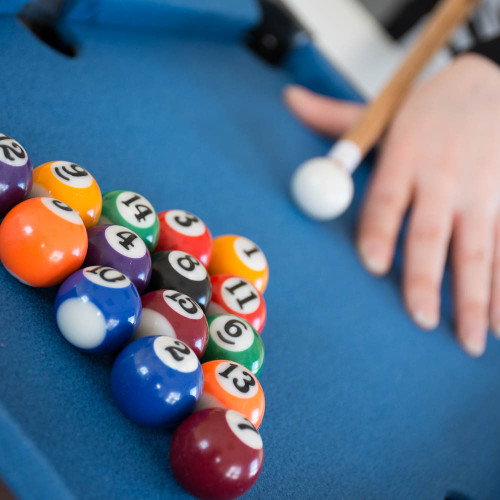 Close-up of a Mini Table Top Pool table, with colourful balls racked and a player lining up a shot on the bright blue surface.