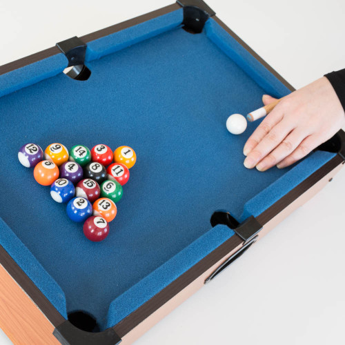 A hand lines up a shot with a cue stick on the Mini Table Top Pool game. The coloured balls are racked and ready for the break.