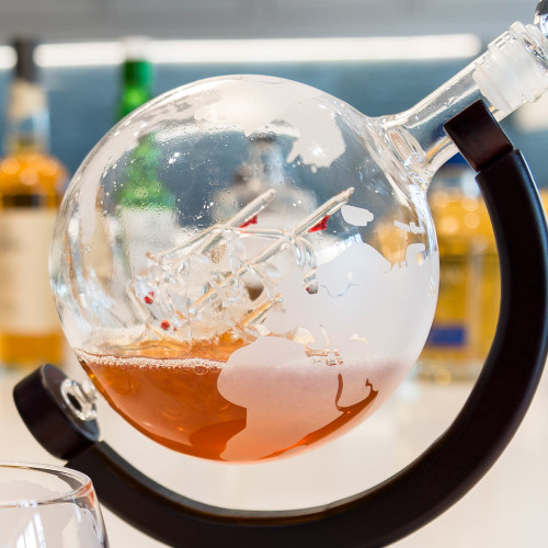 Close-up of a Globe Decanter on its wooden stand, containing a glass ship in amber-coloured spirit.